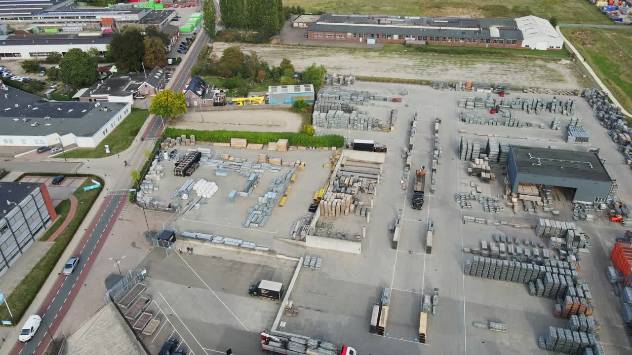 Drone flying over the rooftop of a large company building and revealing a neatly organized storage yard filled with construction materials