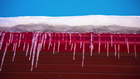 primer plano de un borde del techo cubierto de nieve con los carámbanos adjuntos