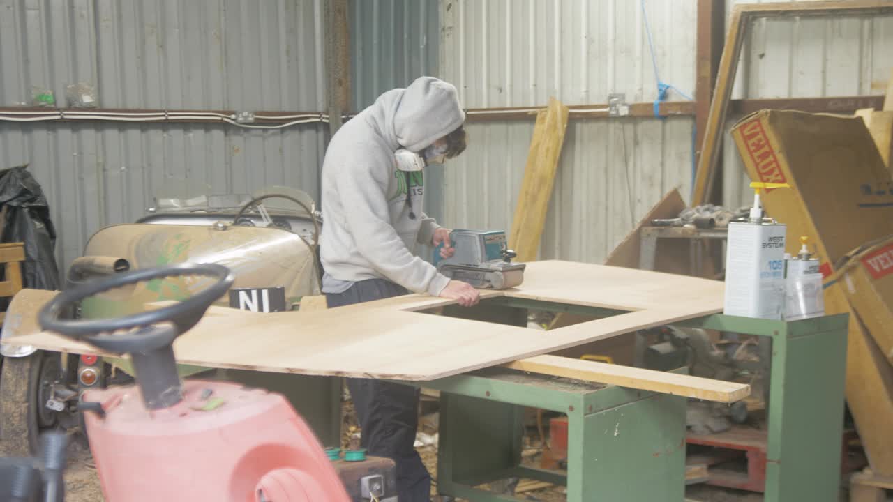 Carpenter sanding plywood with belt sander in garage