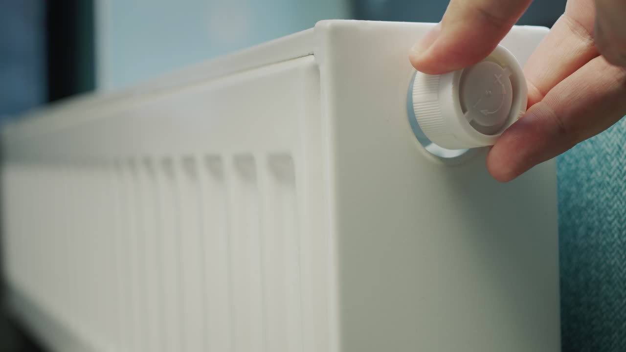A man's hand regulates the temperature on a heating radiator. Conservation of energy resources in a private house
