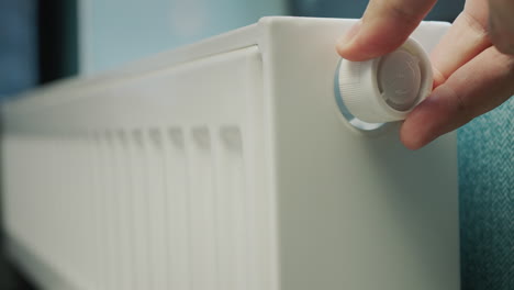 la mano de un hombre regula la temperatura de un radiador de calefacción. conservación de recursos energéticos en una casa particular