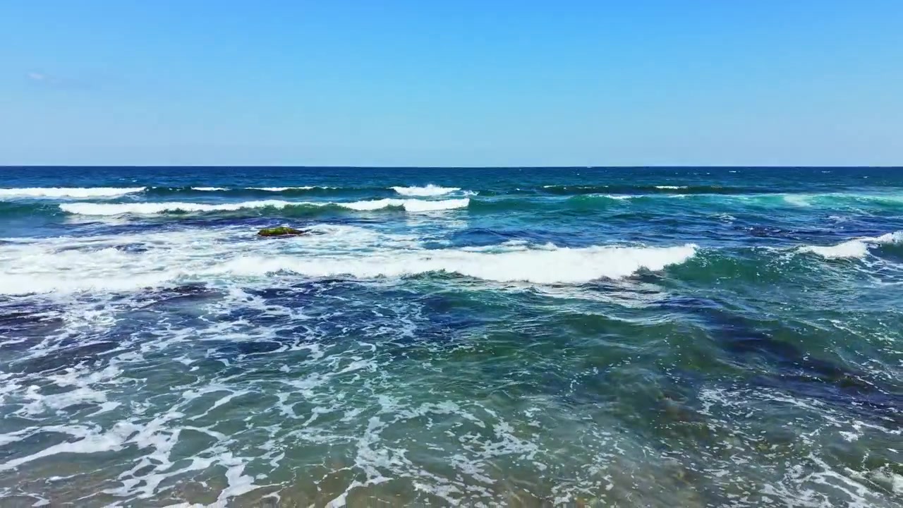 Le onde si infrangono sulla riva dell'oceano sotto un cielo azzurro limpido durante il giorno