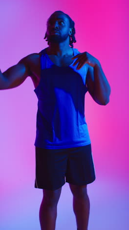 vertical video studio portrait of male basketball player wearing team vest throwing and catching ball against colourful low key mixed lighting