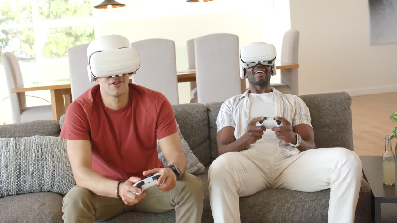 Diverse male friends settling on couch at home donning VR headsets and using controllers for gaming