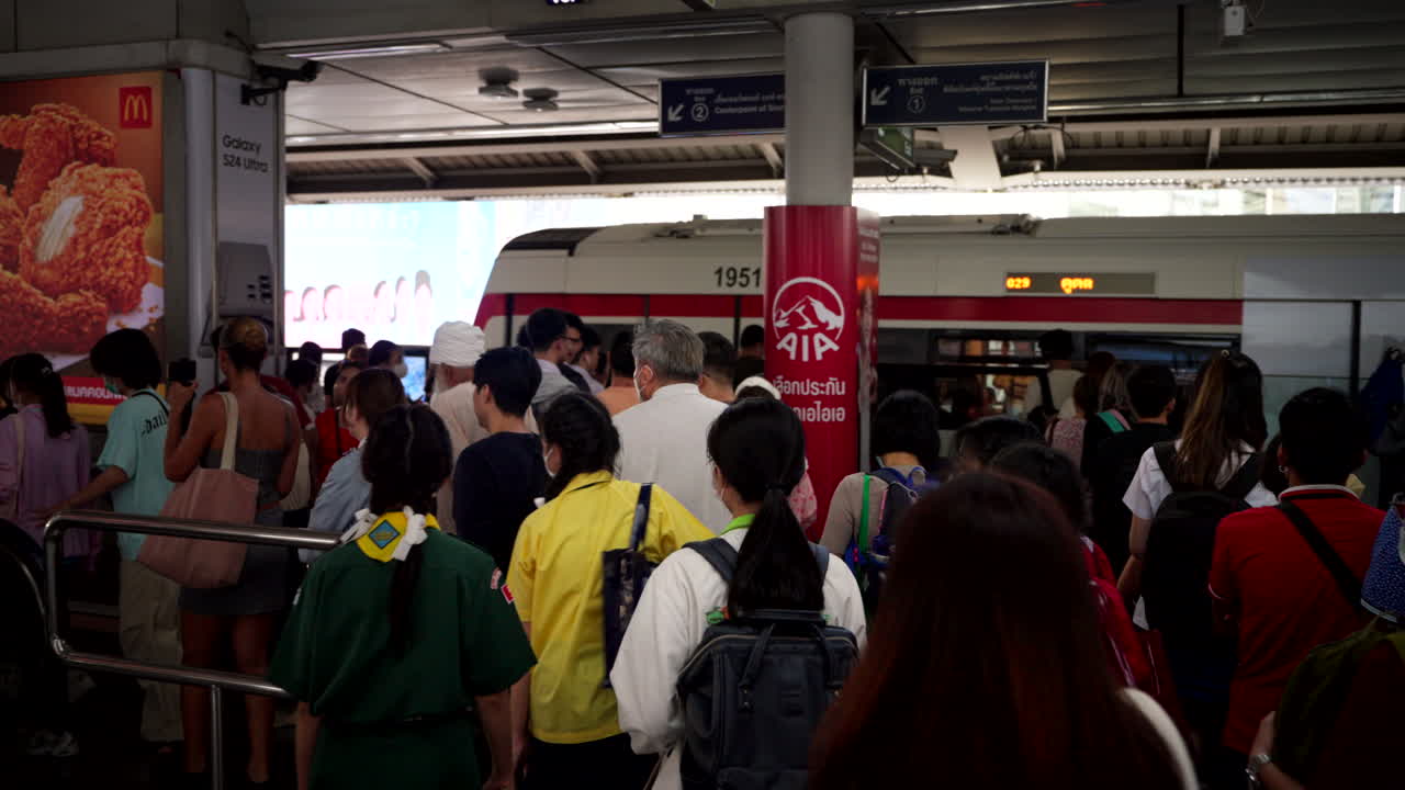 Tourists and locals rush through crowded packed Skytrain station, bustling commuters and trains arriving