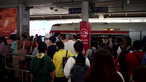 tourists and locals rush through crowded packed skytrain station, bustling commuters and trains arriving