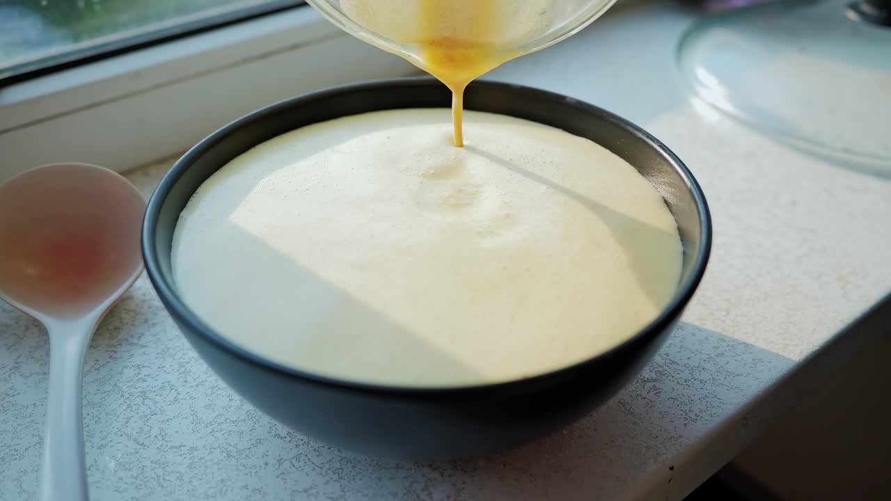 Creamy pancake batter slowly poured into bowl in bright, cozy kitchen corner