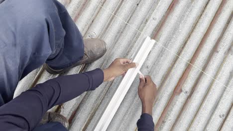 una vista azimutal de un trabajador apretando un perno en un riel de soporte de panel fotovoltaico de aluminio en un techo ligeramente oxidado