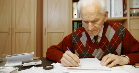 senior businessman writing on paper at table in office 16