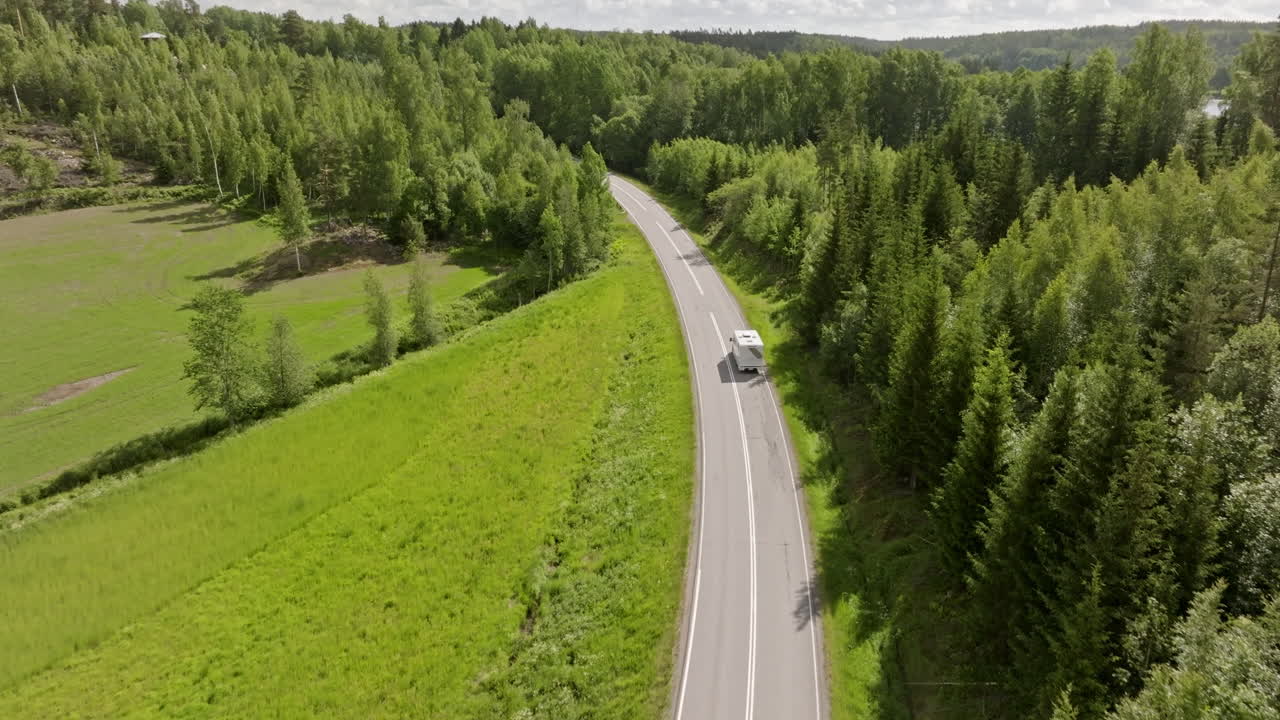 Aerial view following a camper van driving on a rural forest road, summer day