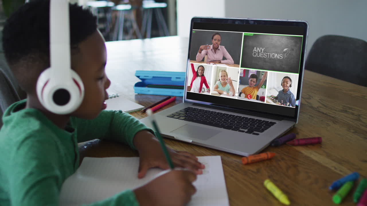 Schoolboy using laptop for online lesson at home, with diverse teacher and class on screen