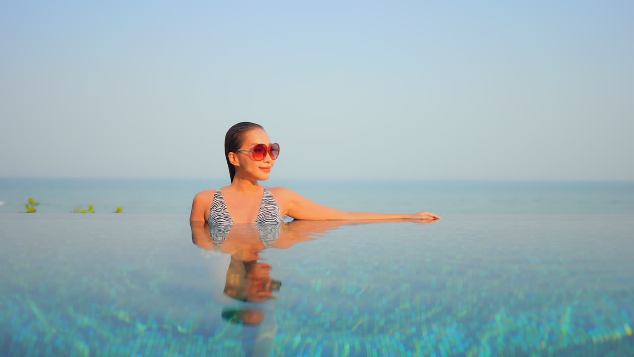 A young attractive woman leans against the edge of an infinity pool ...
