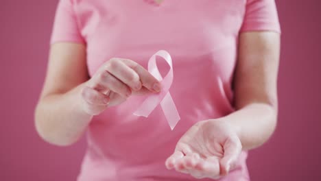 Mid-section-of-woman-holding-a-pink-ribbon-against-pink-background