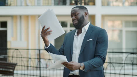 un hombre de negocios afroamericano decepcionado leyendo documentos al aire libre.