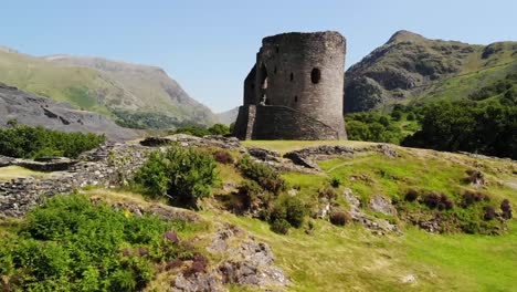 Aerial-shot-of-castle-ruins-in-Wales,-shot-on-a-sunny-and-warm-day-with-the-beautiful-countryside-in-the-background-including-a-lake,-rolling-hills,-and-trees