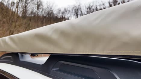 slow motion clip panning down the side of a camping awning mounted to the side of a white all-terrain suv on a dreary day