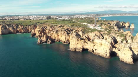 Ponta-da-Piedade-lighthouse-surrounded-by-barren-headlands-in-Algarve---Wide-Aerial-top-view-slow-Orbit-shot