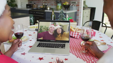 pareja afroamericana con vino usando computadora portátil para la videollamada de navidad con pareja en la pantalla