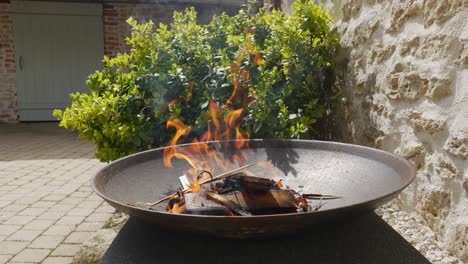 round iron pit with flames flickering and hand throwing wood onto fire