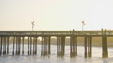 Toma-Panorámica-De-Personas-Caminando-Por-El-Muelle-De-Ventura-Con-Puesta-De-Sol-En-El-Fondo-Ubicado-En-El-Sur-De-California