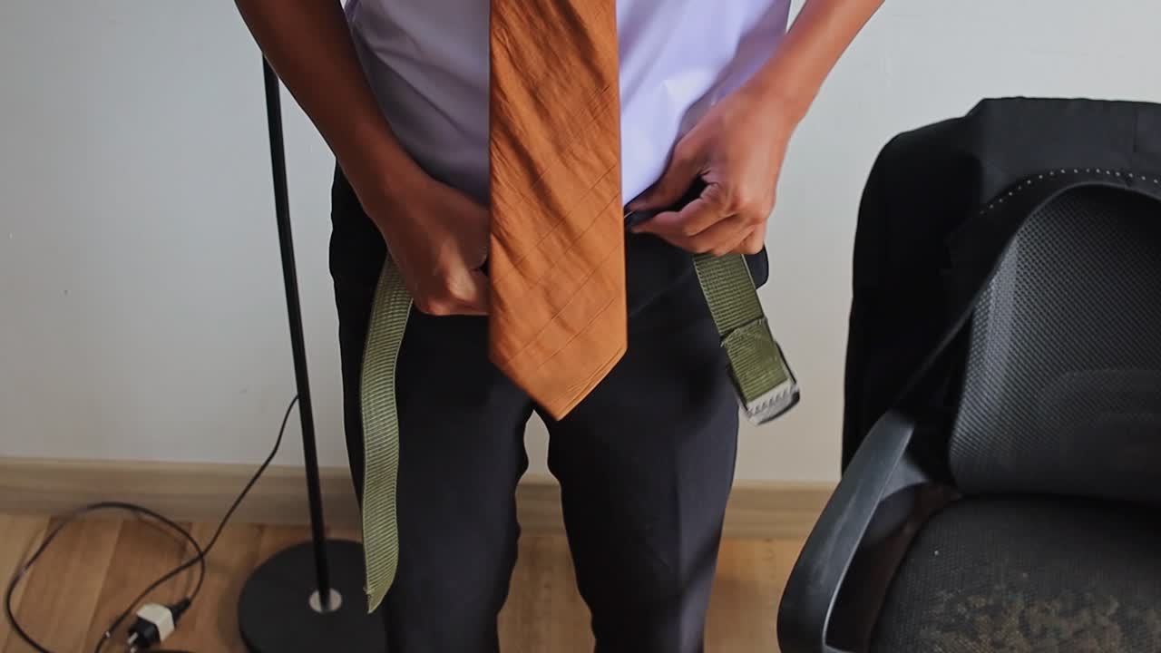 Close-up of businessman fastening black pants and green belt while getting dressed in room