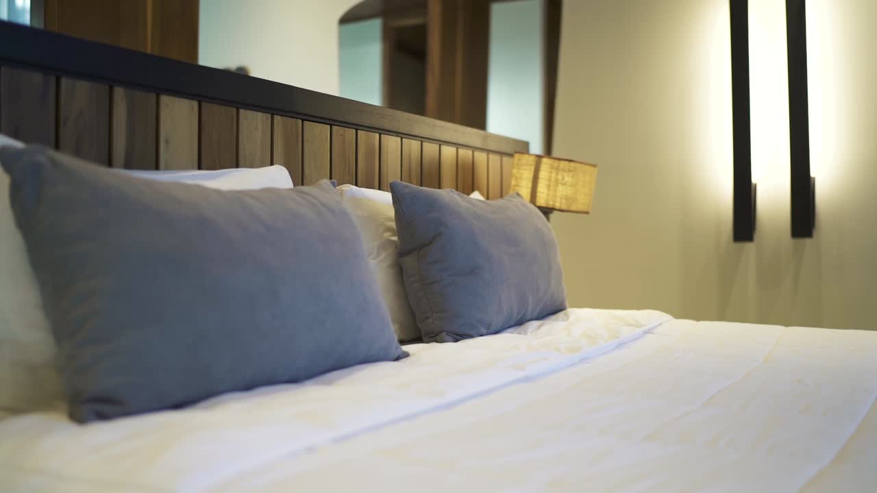 White linens, fluffy pillows and wooden headboard create a cozy and inviting atmosphere in a modern hotel room, perfect for a relaxing stay, slow motion reveal