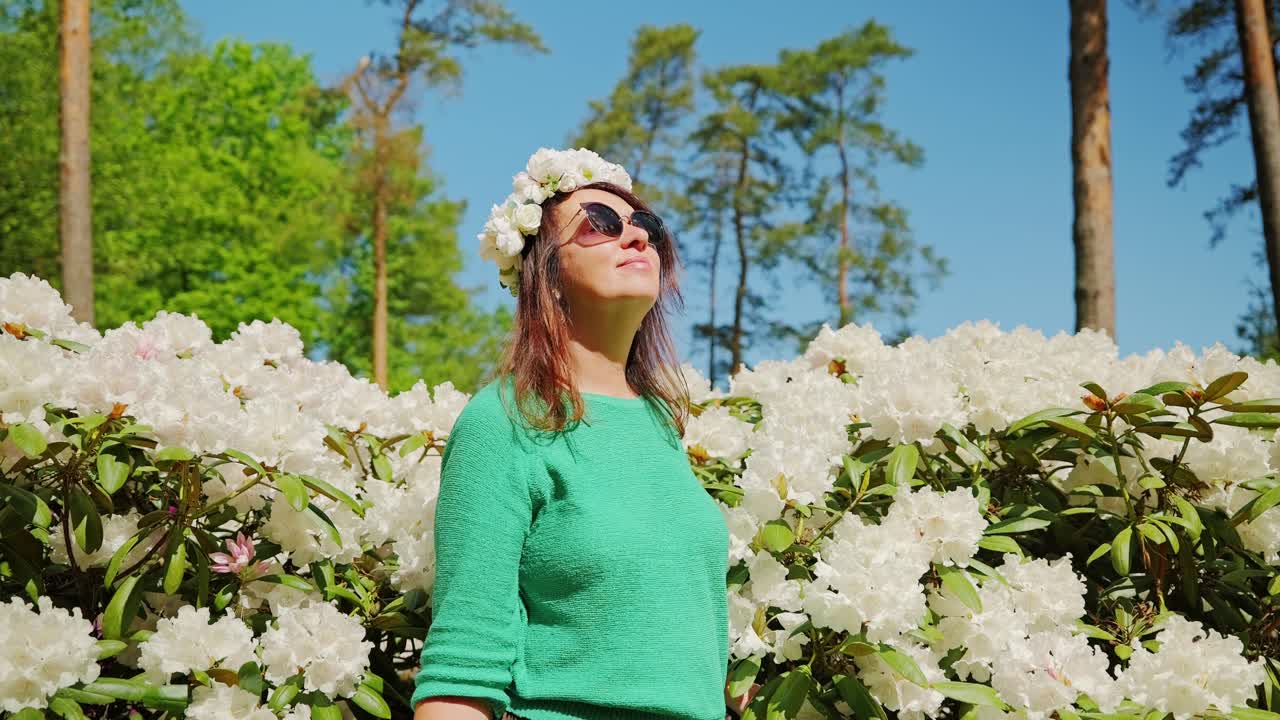 Donna aggraziata con occhiali da sole che si gode una giornata primaverile in un parco fiorito, menopausa.