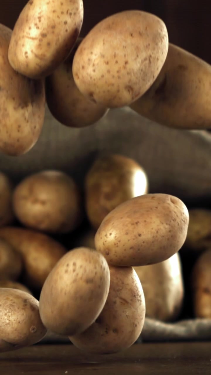 Patate crude che cadono al rallentatore su una superficie di legno