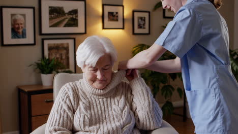 caregiver helps an elderly woman adjust her sweater at home