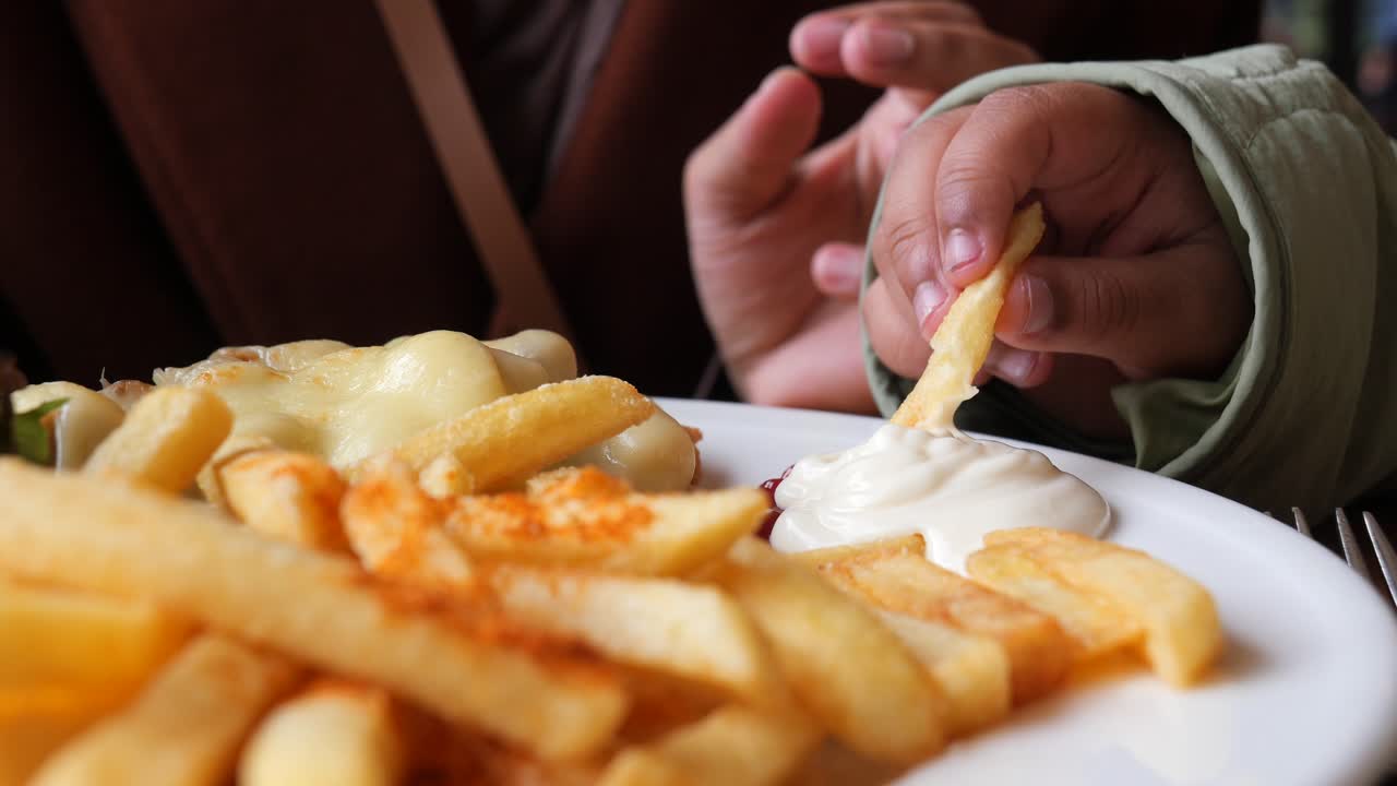Close up of a person's hand reaching for fries and sauce on a plate