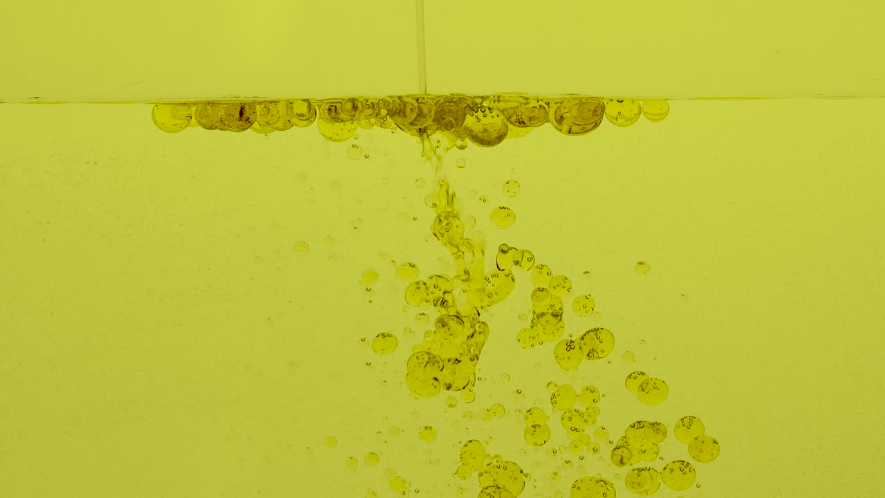 el aceite cae en el líquido amarillo formando bolas que vuelven a la superficie.