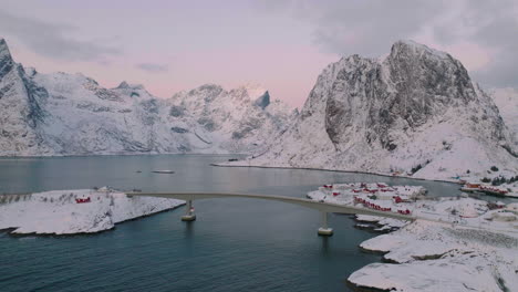 Transport-bridge-crossing-Lofoten-islands-idyllic-remote-village-over-scenic-blue-ocean-aerial-reveal-view