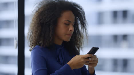 focused african american woman executive looking mobile phone in workplace.