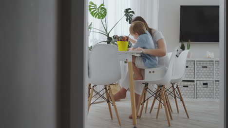 a young mother with two children sitting at a white table draws colored pencils on paper in slow motion