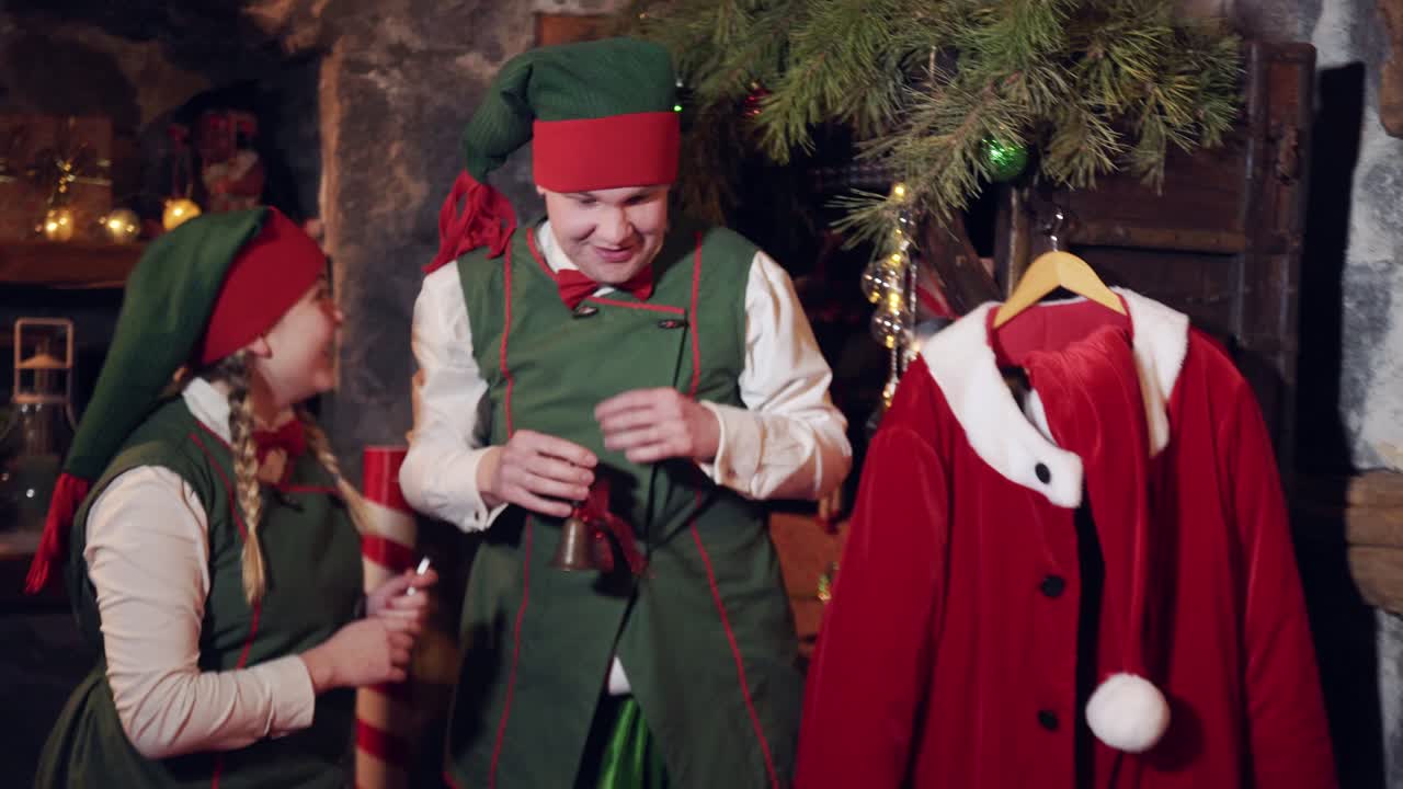 Naughty elves with a bell waking Santa. Funny elves ringing with a little bell over Santa sleeping in his bed at Christmas eve