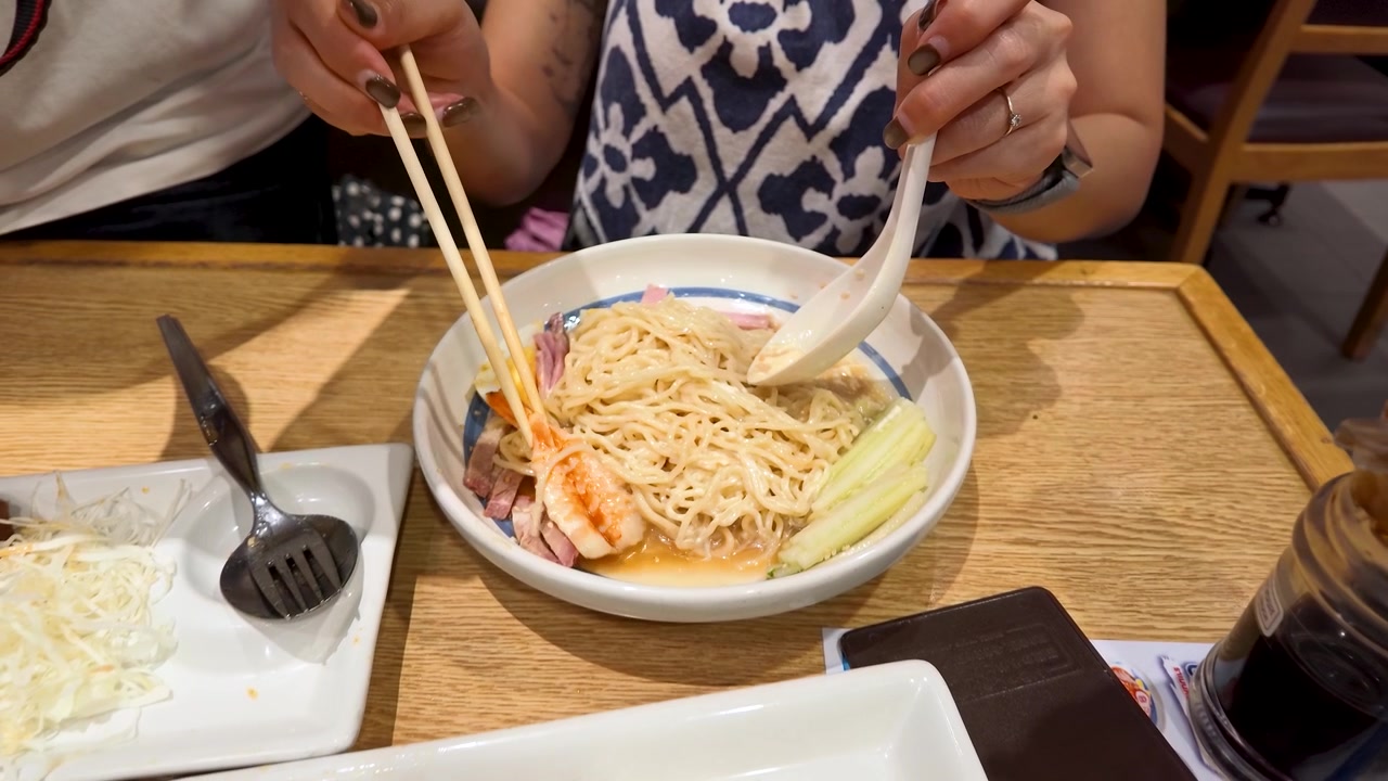 Primo piano di donna che usa bacchette e cucchiaio per mangiare ramen a un tavolo di legno