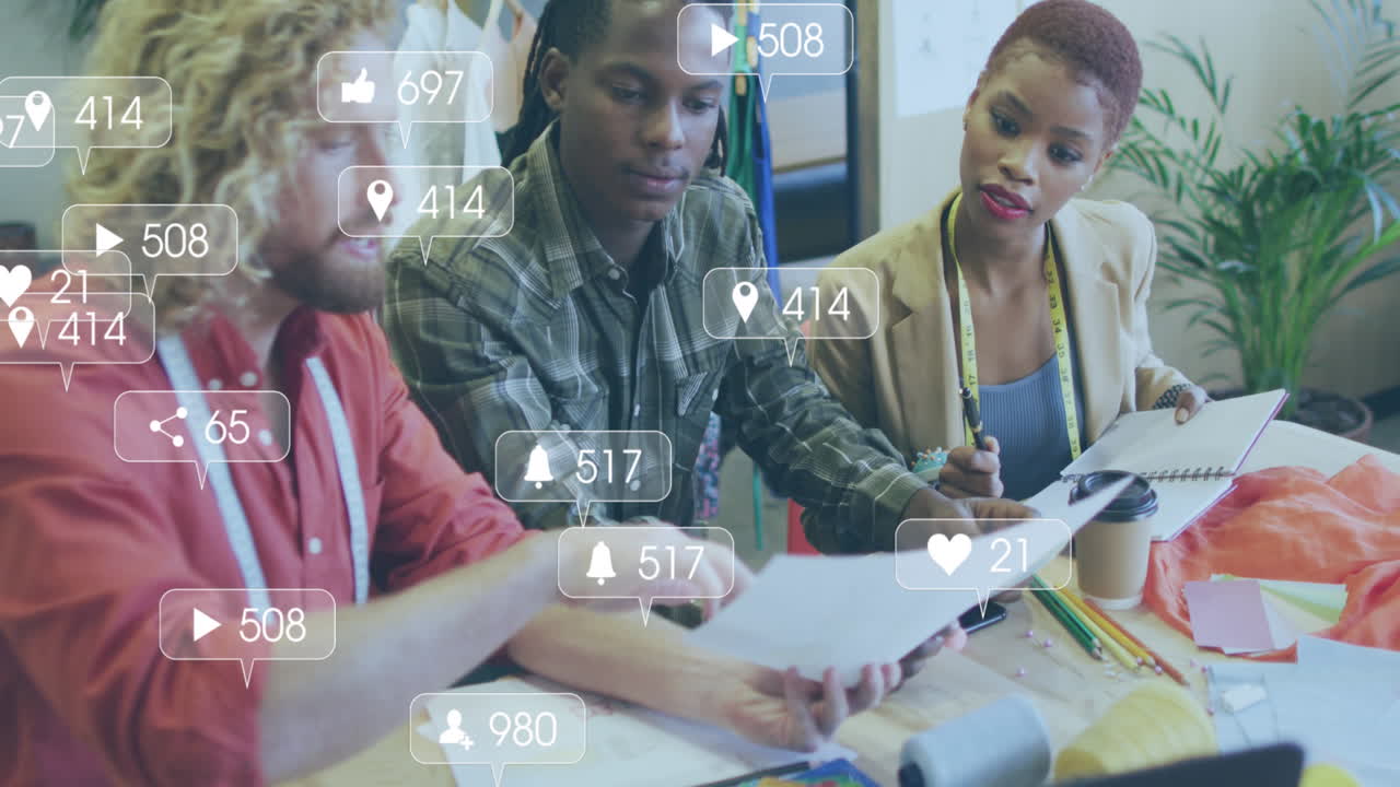 Animation of social media icons against team of diverse fashion designers discussing at office