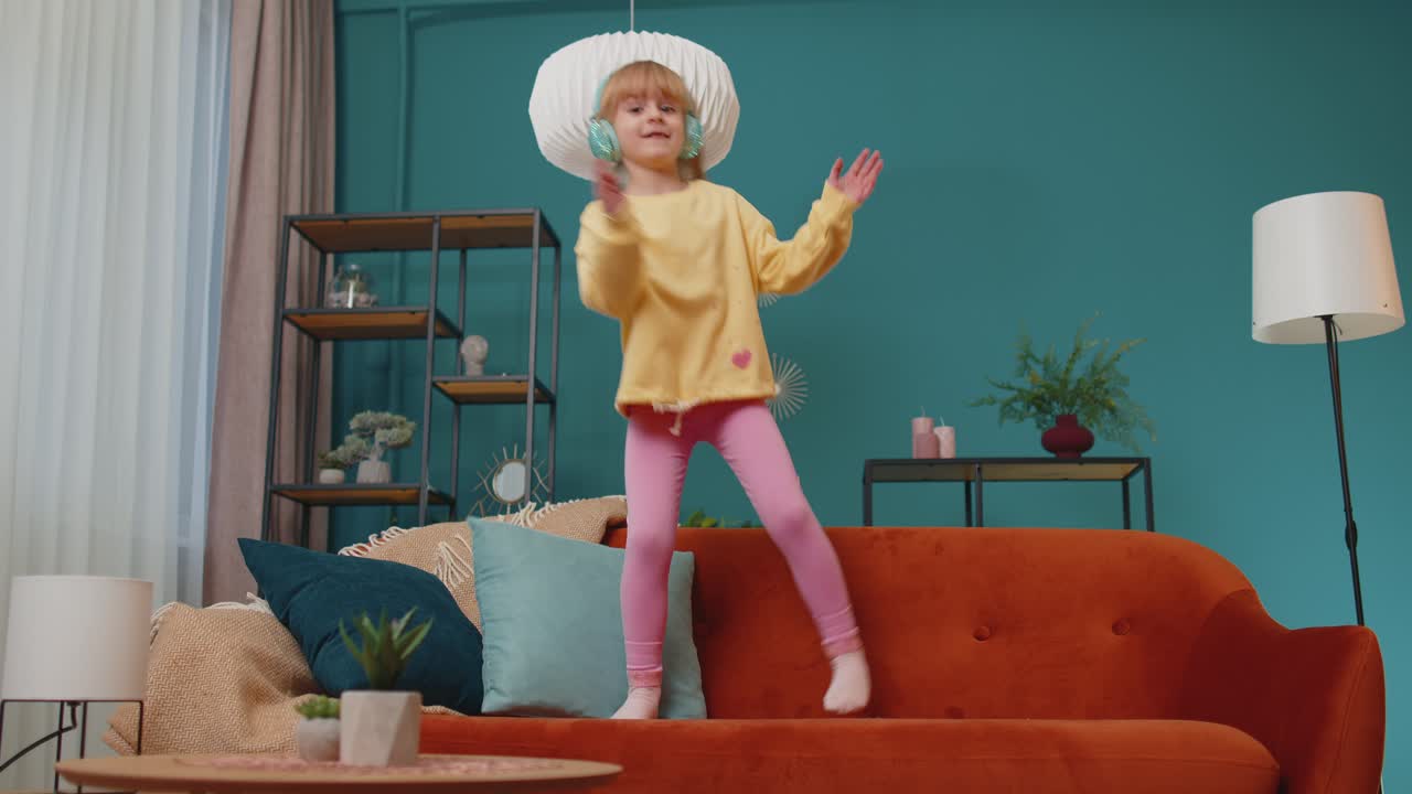 Happy child girl kid in headphones dancing and jumping while listening to the music at home alone