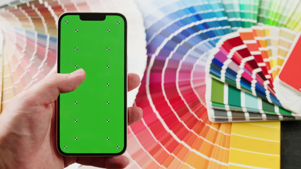 mano sosteniendo un teléfono inteligente con pantalla verde, frente a muestras de color
