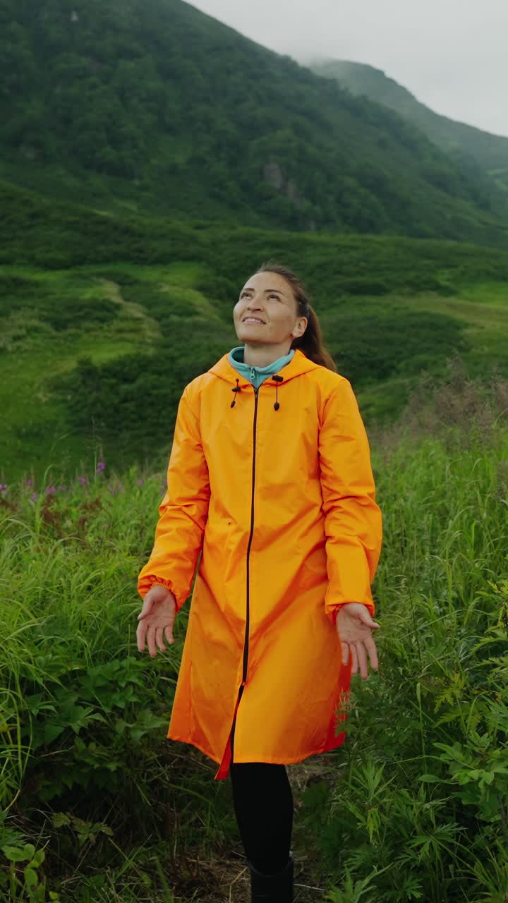 Donna felice con impermeabile arancione che si gode la natura tra le montagne verdi