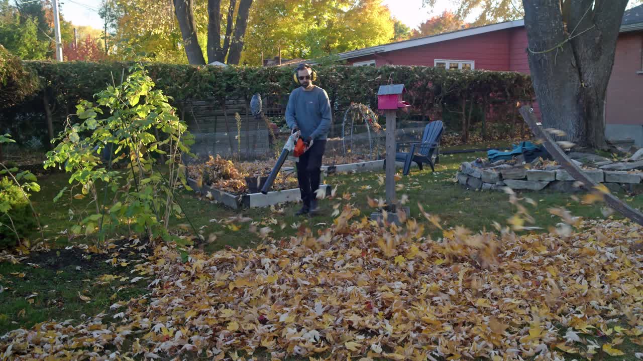Man in backyard blows a scattering of leaves with a gas leaf blower