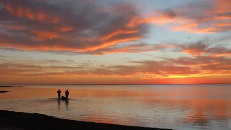 two people wade into tranquil laguna madres estuary while towing fishing gear in a small boat during a colorful sunset