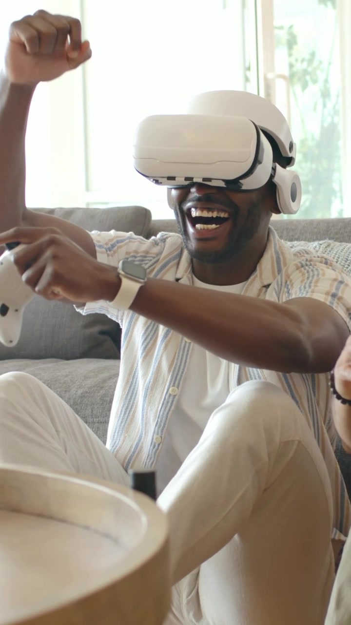 Amici che giocano indossando maglietta rossa e camicia a righe usando visori VR bianchi e controller sul divano