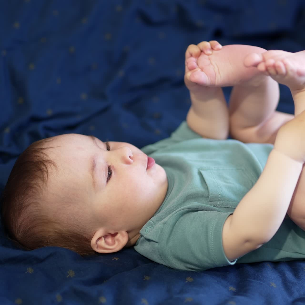 Healthy Caucasian kid plays with his bare feet lying on sofa. Beautiful baby pulls his feet to face. Close up