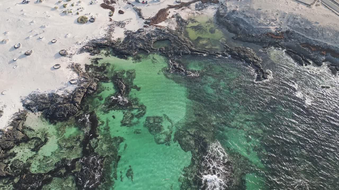 Drone footage of the rugged coastline in El Cotillo, Fuerteventura, with waves crashing over volcanic rocks and deep blue Atlantic water.