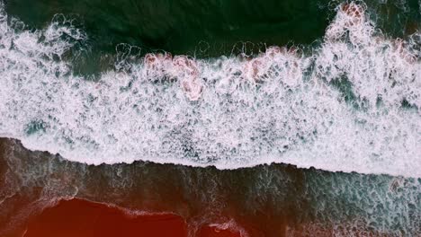 Vista-Aérea-De-Una-Ola-Rompiendo-En-Una-Playa-De-Arena-Dorada,-Los-Fascinantes-Patrones-De-Espuma-Y-Surf