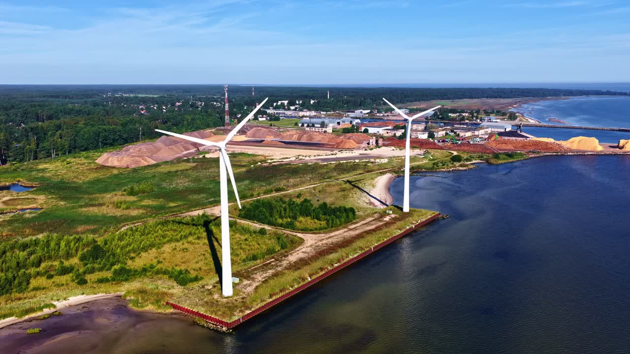 Waterfront wind power plant under clear sky and sunny daylight, forest in background, Aerial