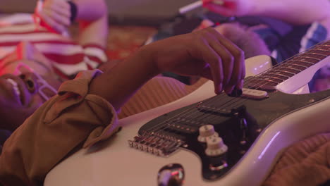 close up of girl playing guitar while lying on floor in circle with friends during rehearsal in recording studio