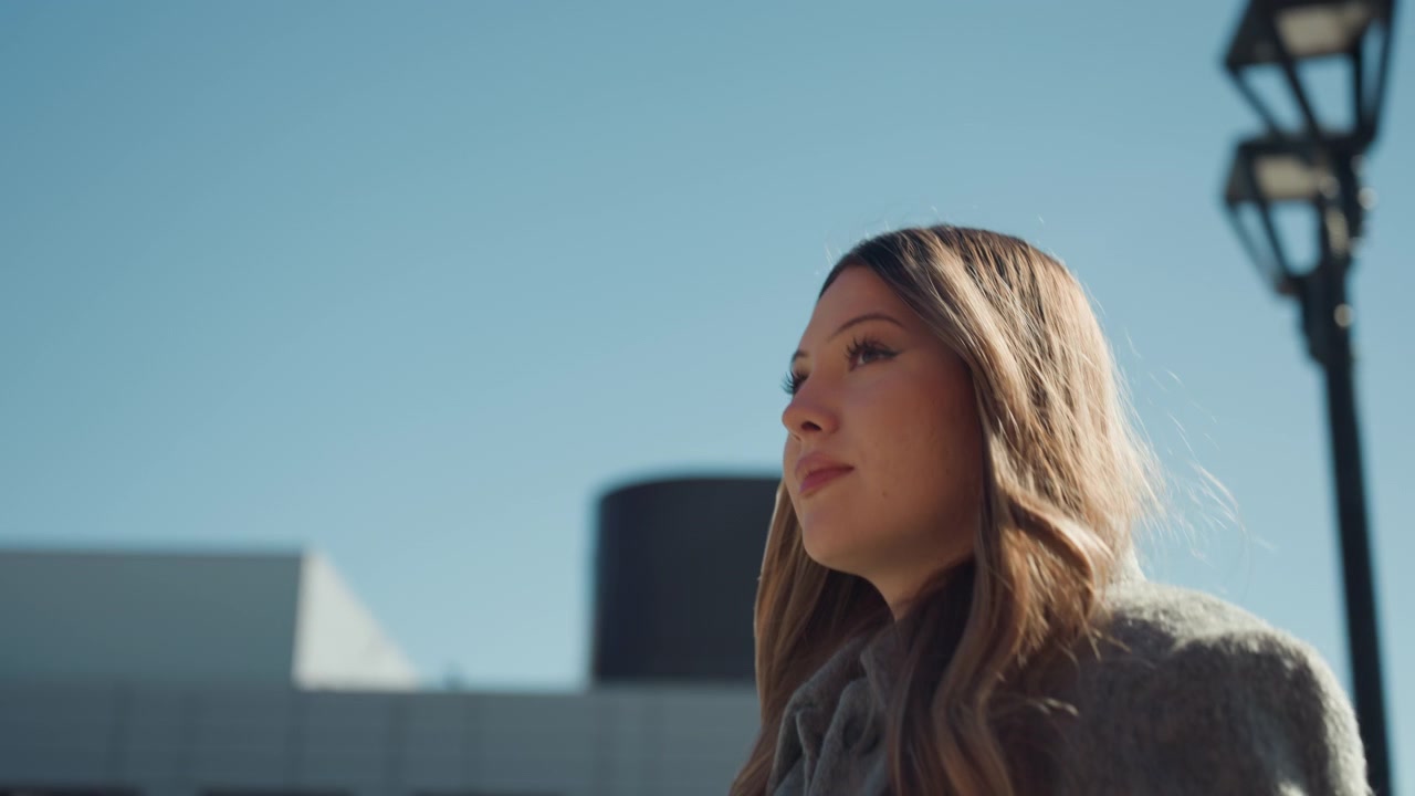 Pretty caucasian woman looking upward toward sky, confident entrepreneur posture, modern architecture backdrop, sunlight highlighting hair, serene expression, empowered mood, closeup composition