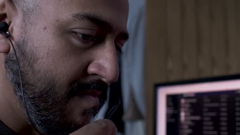 a close up shot of an indian man working from home talking into the microphone of his mobile phone headset, his face animated as he converses with the caller discussing details